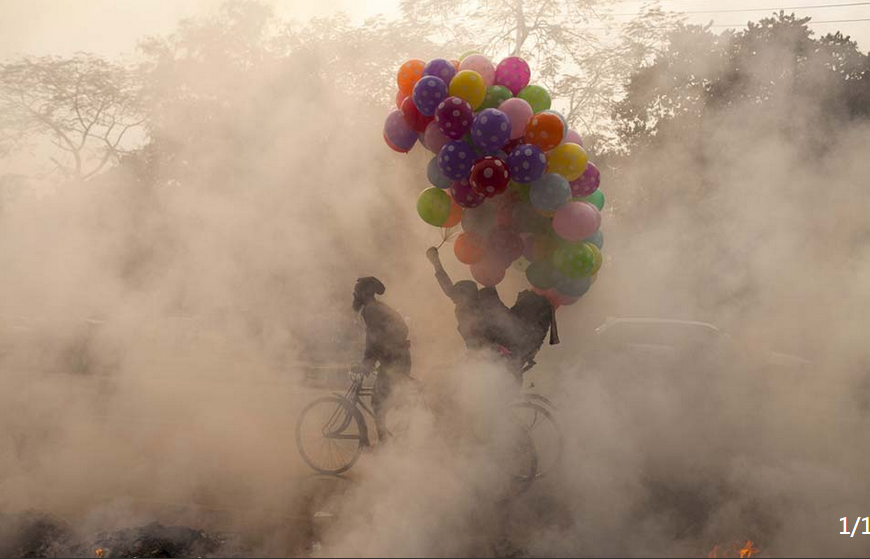 当地时间2016年1月29日，孟加拉国达卡，一名男子骑自行车穿过由垃圾焚烧引起的浓烟中。.png